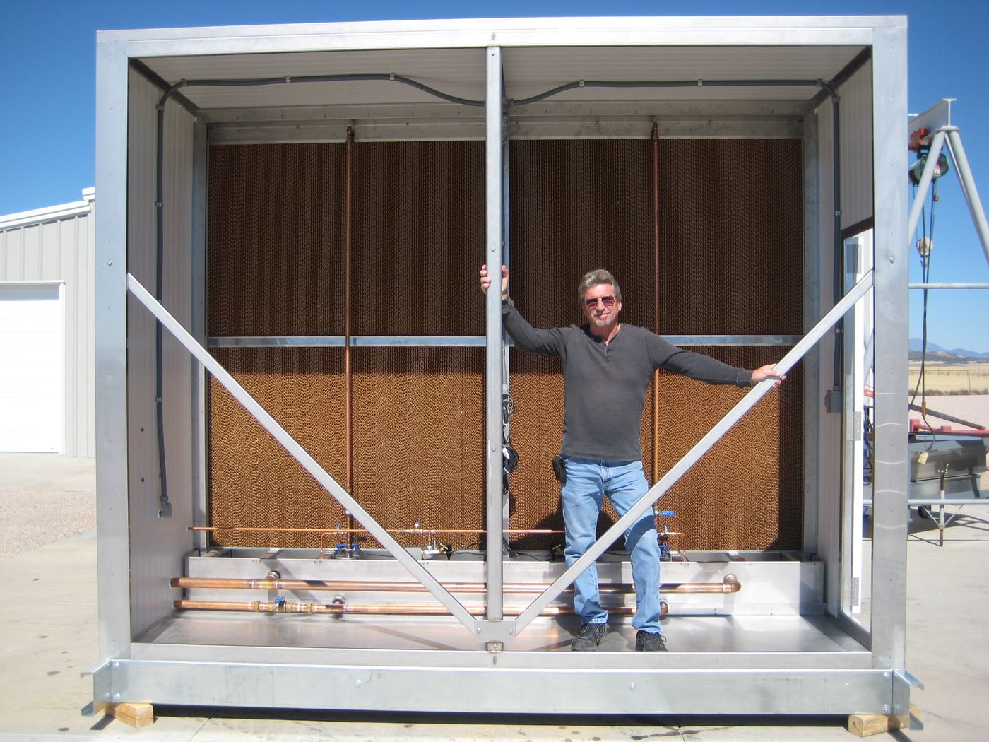 A person standing inside a large insulated evaporative cooler housing, in front of two stacked banks of rigid media