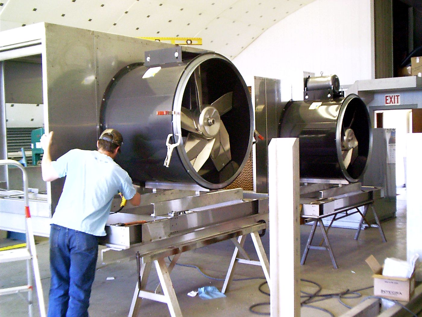A worker assembling a large stainless steel cooler fitted with two tube axial blowers